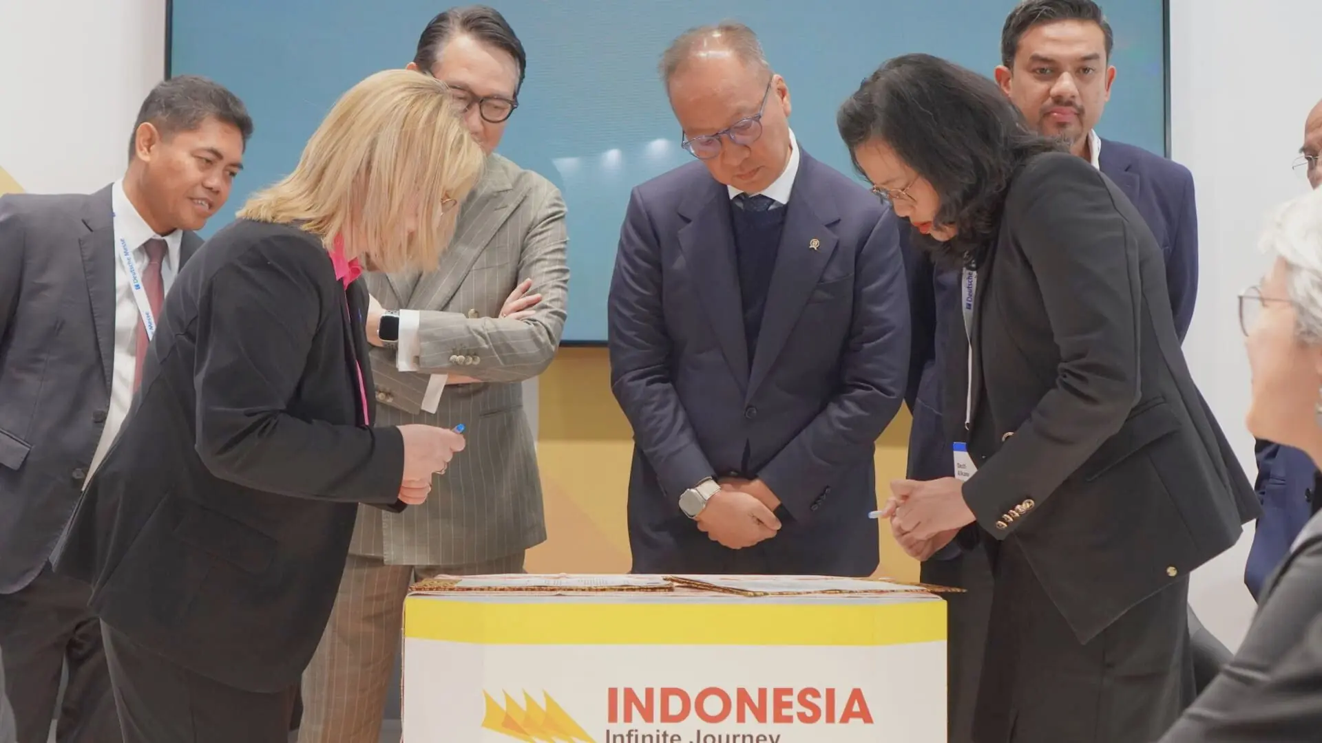 Two executives, one from ECADIN and another from TUV NORD CERT, seated at a polished conference table, exchanging signed documents with satisfied smiles. In the background, a banner displaying "Sustainable Industry Indonesia" hangs prominently, symbolizing the collaborative effort towards sustainability in the industrial sector. Bright, natural light floods the room, evoking a sense of clarity and transparency in the partnership.