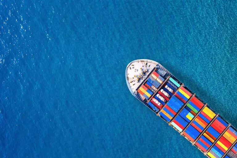 Aerial view of a large cargo ship sailing in open blue waters, symbolizing international maritime trade. This image represents the global push toward decarbonization as the IMO approves net-zero shipping regulations 2025, including a new carbon pricing framework for ships over 5,000 gross tonnage.